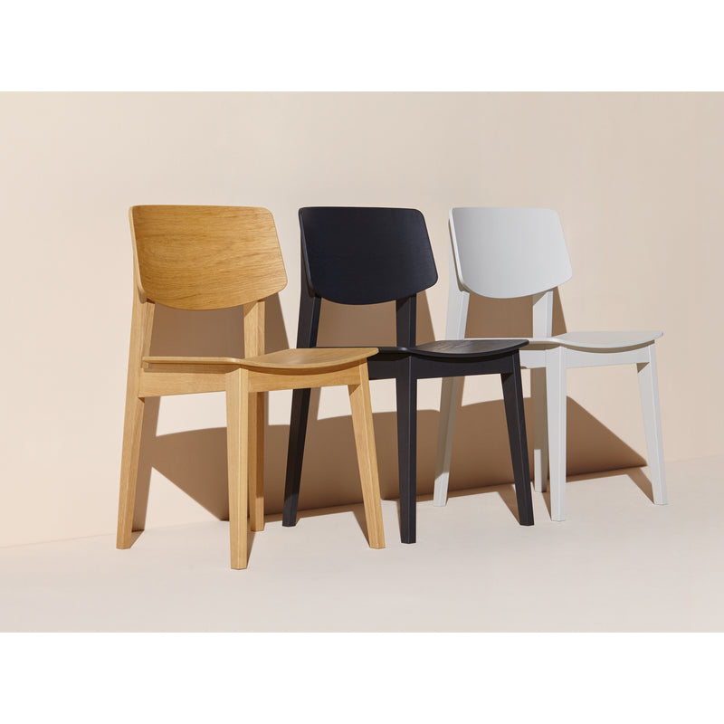 Three Usus Chairs by Bartmann Berlin, in oak, black, and white finishes, are arranged in a row against a beige background. Their minimalist design and clean lines exude natural elegance that embodies Bartmann Berlins signature style.