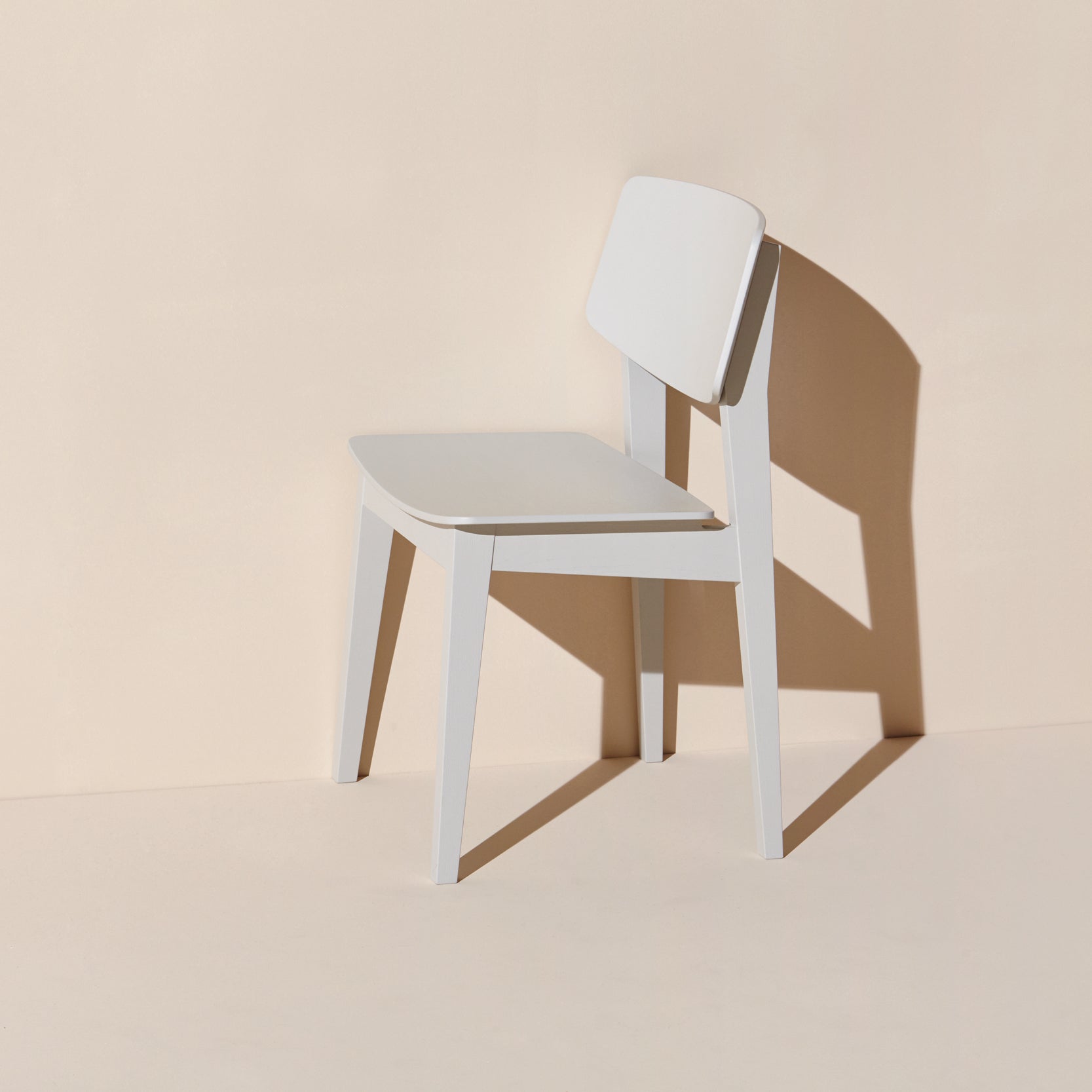 The Usus Chair by Bartmann Berlin showcases natural elegance against a beige backdrop. A sleek minimalist white design with clean lines is accentuated by the light, embodying contemporary style and refined aesthetic.