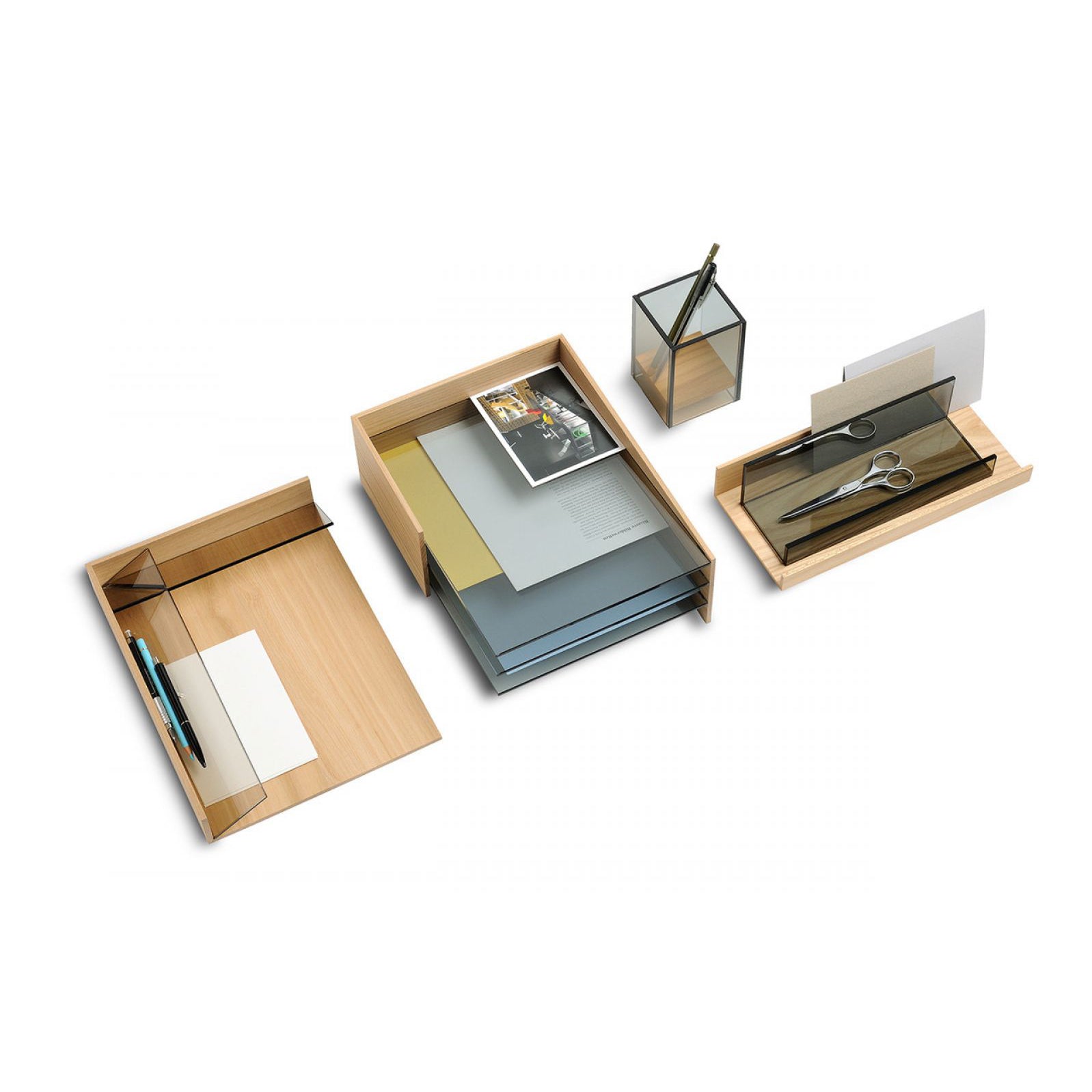The Charlie Desk Accessories by Boewer, designed by Pauline Deltour, feature elm and colored glass elements. It includes wooden trays for documents, a ruler, scissors, pens, and a photo. A tall pen holder keeps everything organized on a pristine white surface.