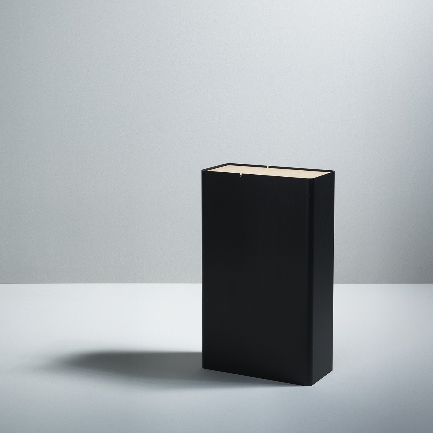 A minimalist P-3 by Boewer stands upright on a light gray surface against a matching background, akin to an aluminum containers sleek design. The black cover is plain with no visible text or graphics, casting a soft shadow to the left.