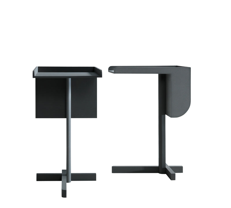 These minimalist side tables from Boewers School collection echo Konstantin Grcics functional elegance. With dark gray finishes, one has a rectangular top and flat side while the other is rounded, both perched on cross-shaped bases with unique geometries.