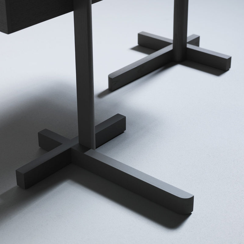 A close-up of Boewers School table showcases its two dark cross-shaped legs on a light gray floor, creating a minimalist and stylish contrast reminiscent of Konstantin Grcics modern aesthetic.