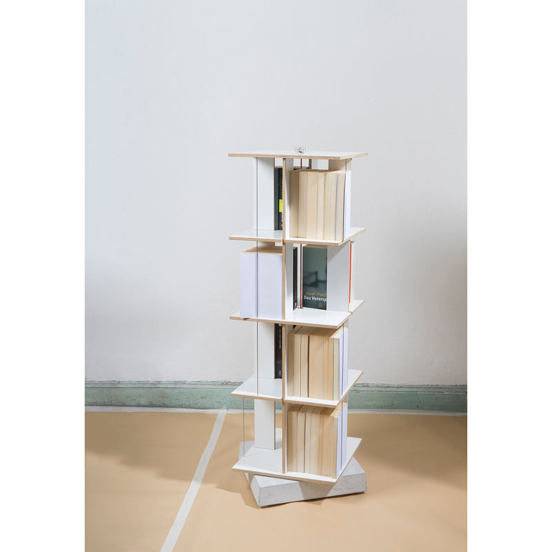 The Buchstabler bookshelf by Moormann is a tall, uniquely designed piece with three pivotable tiers. Each section can be rotated, displaying colorful books against a minimalistic white and beige backdrop. Its space-saving base features a gray, angular design.