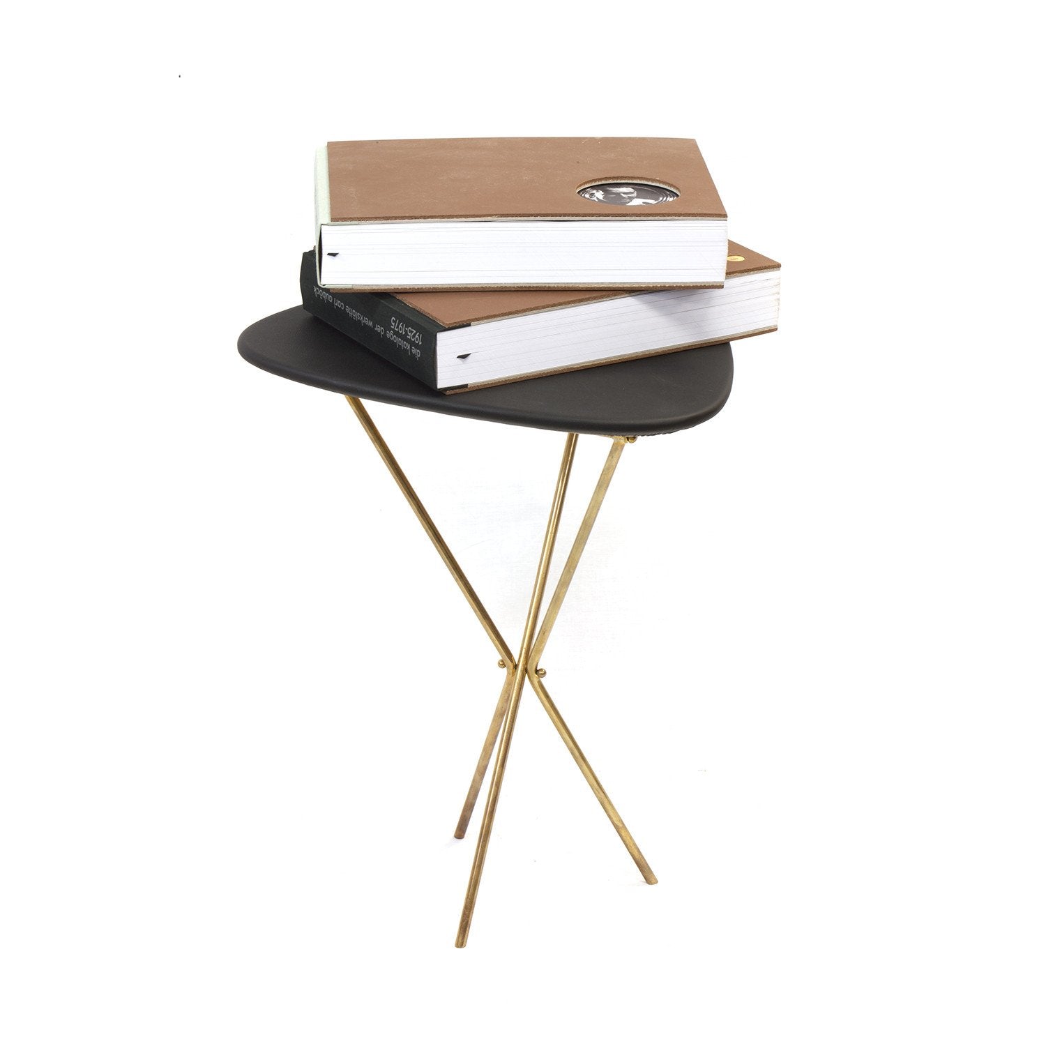 The Sidetable #3642 from Werkstätte Carl Auböck features thin gold legs and a small round design, evoking a Viennese townhouse elegance. Topped with two large hardcover books—a brown-covered one atop another with a black spine—it brings sophistication to any décor.