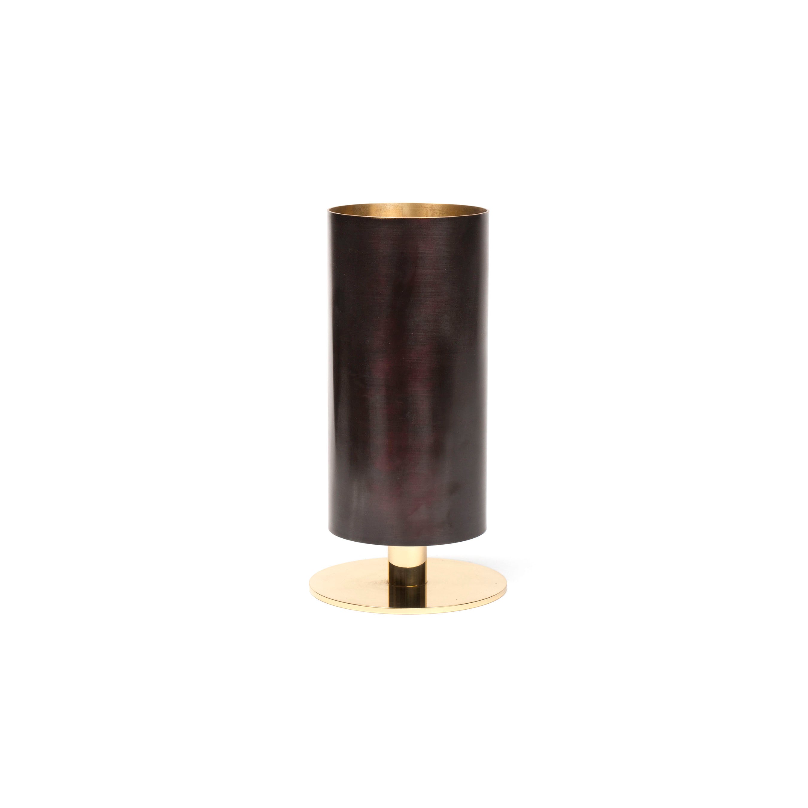 Vase #7247 by Werkstätte Carl Auböck is a tall, cylindrical vase with a dark, smooth surface on a round gold base, exuding modern elegance like Viennese workshop designs against a plain white background.