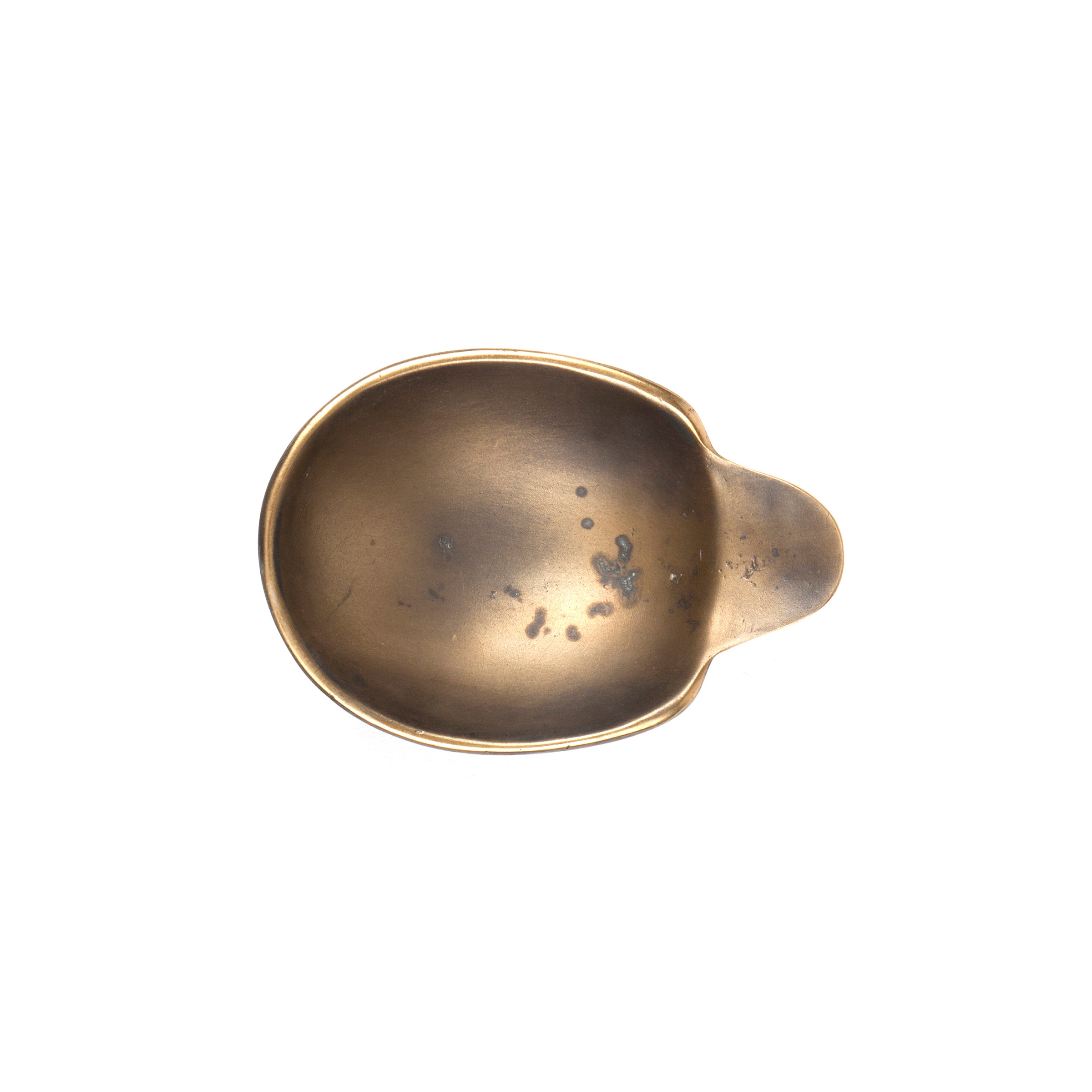 A top-down view of Dish #3599 by Werkstätte Carl Auböck, featuring a vintage, tarnished brass scoop with a short handle on a plain white background. Its round shape shows wear and dark spots, capturing the elegance of a Viennese townhouse.