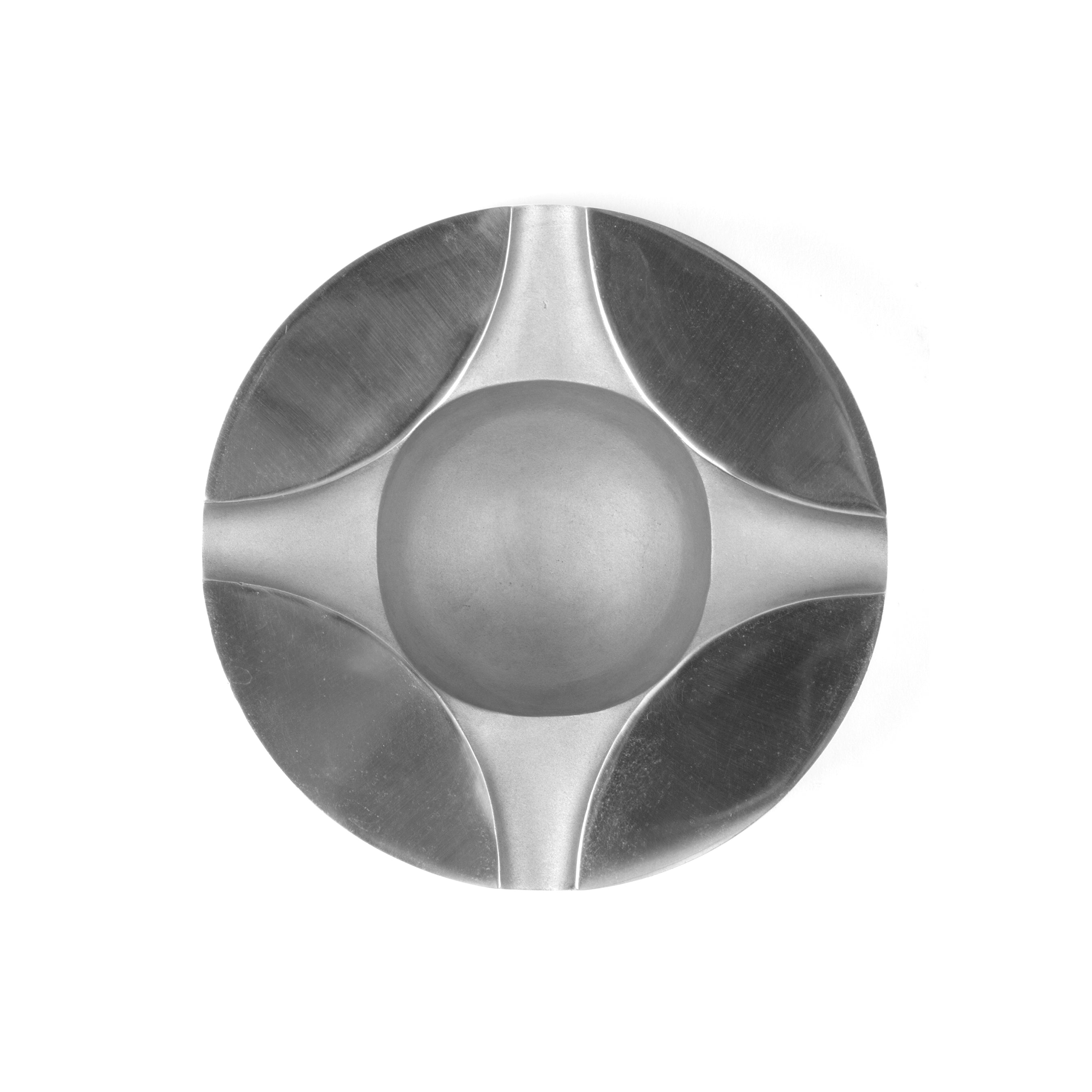 The Werkstätte Carl Auböck Ashtray #5556-1 is a round, silver, polished bowl with a futuristic design featuring smooth, raised center and symmetrical elongated petal-like shapes in a cross pattern, reflecting the innovative style seen at the Triennale di Milano.