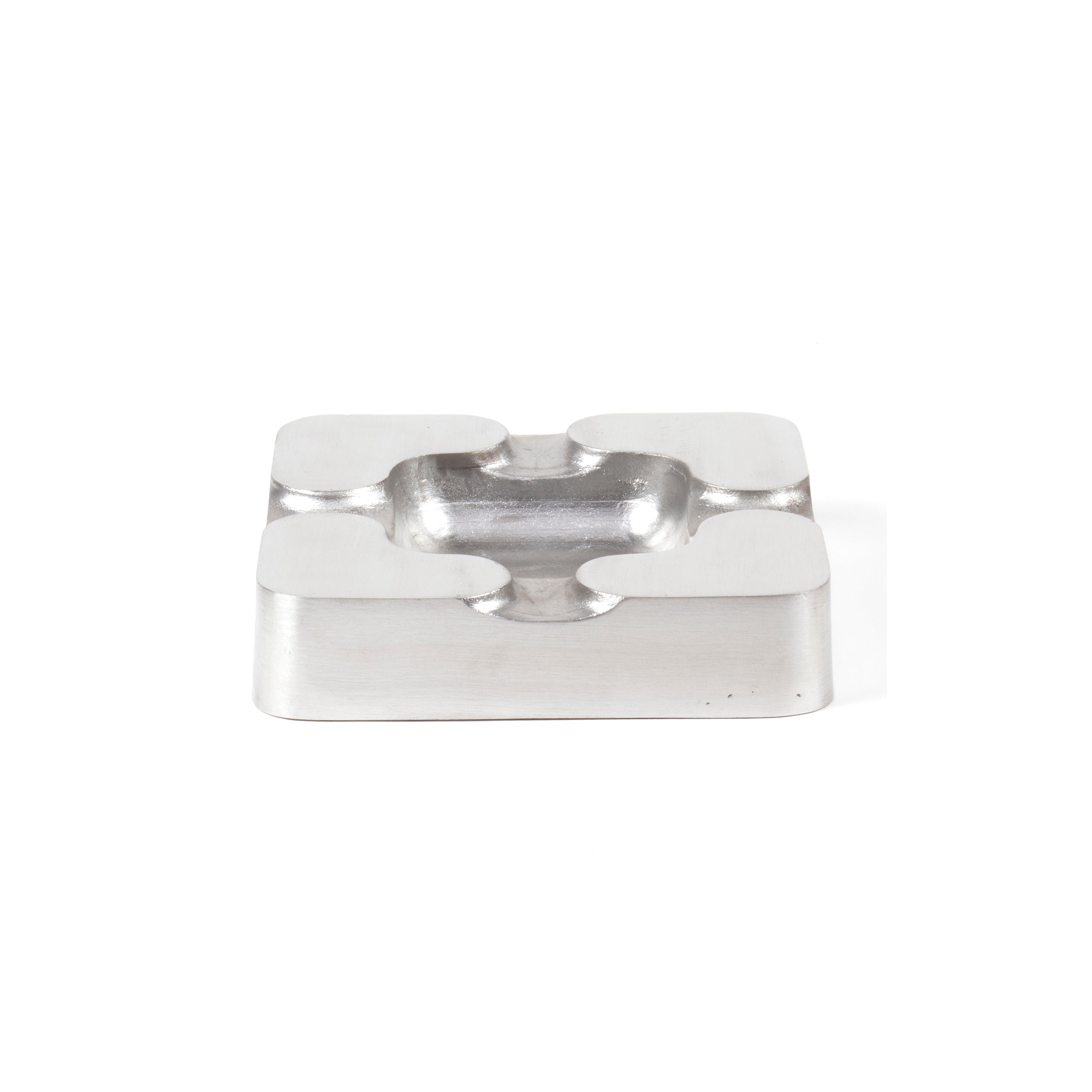 The Ashtray #5556-2 by Werkstätte Carl Auböck is a modern, minimalist stainless steel piece with a square shape, rounded edges, four cigarette grooves, and a central ash depression, elegantly set against a simple white background.