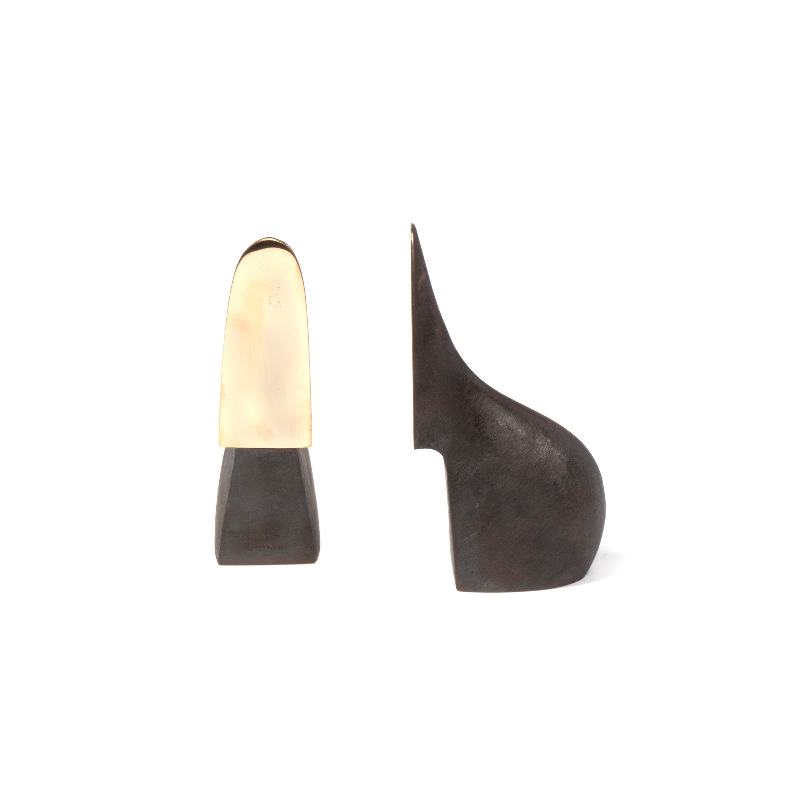 The Pair of Bookends #3652 by Werkstätte Carl Auböck evoke the elegance of a Triennale di Milano exhibit against a white backdrop: one is an elongated gold form with a dark base, and the other is a sleek, dark curved piece reminiscent of Wiener Bronzen.