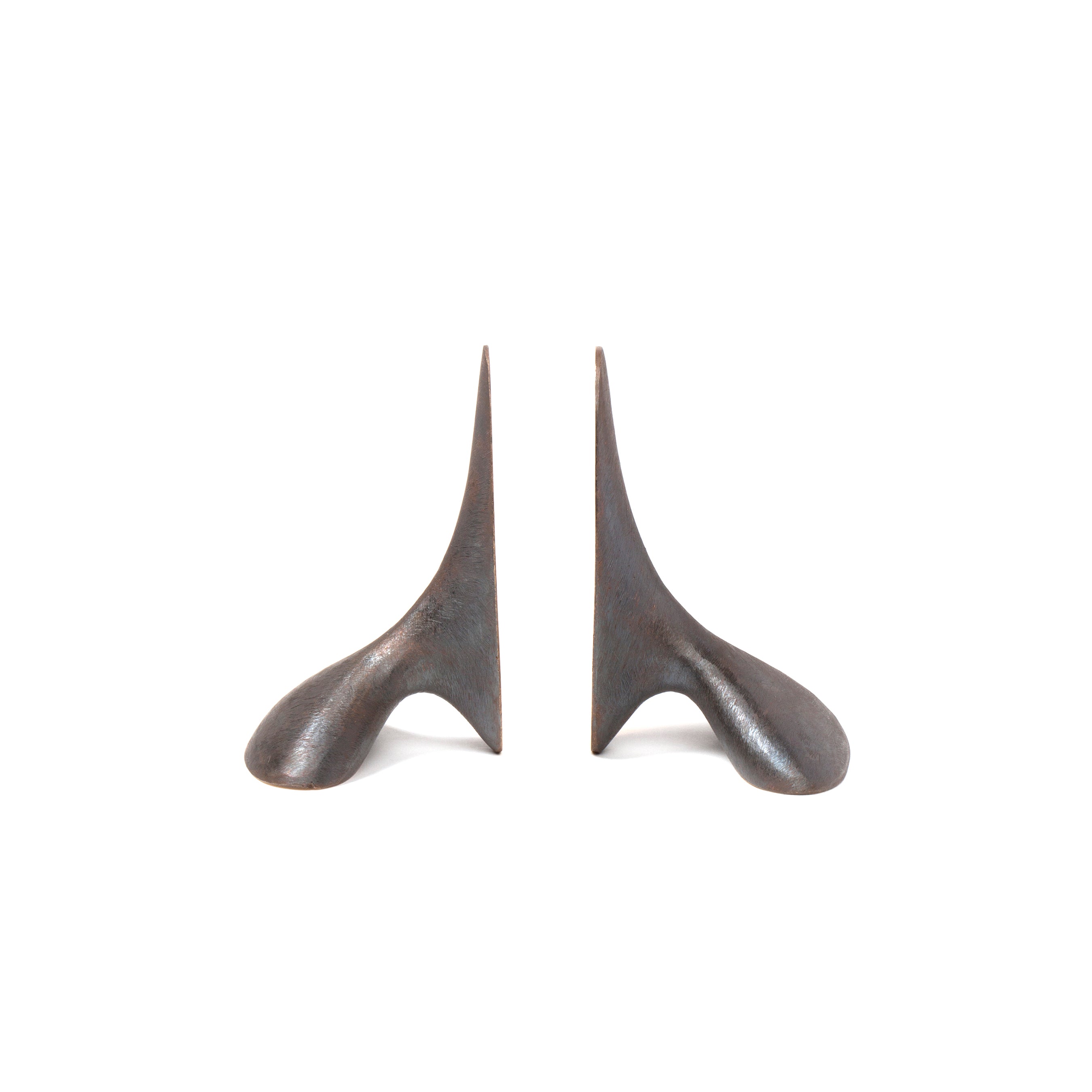 The Pair of Bookends #3653 by Werkstätte Carl Auböck features two identical abstract sculptures with dark metal, curved, pointed shapes on a white background, resembling modern art and echoing the innovative spirit of the Triennale di Milano with broad bases narrowing to points.