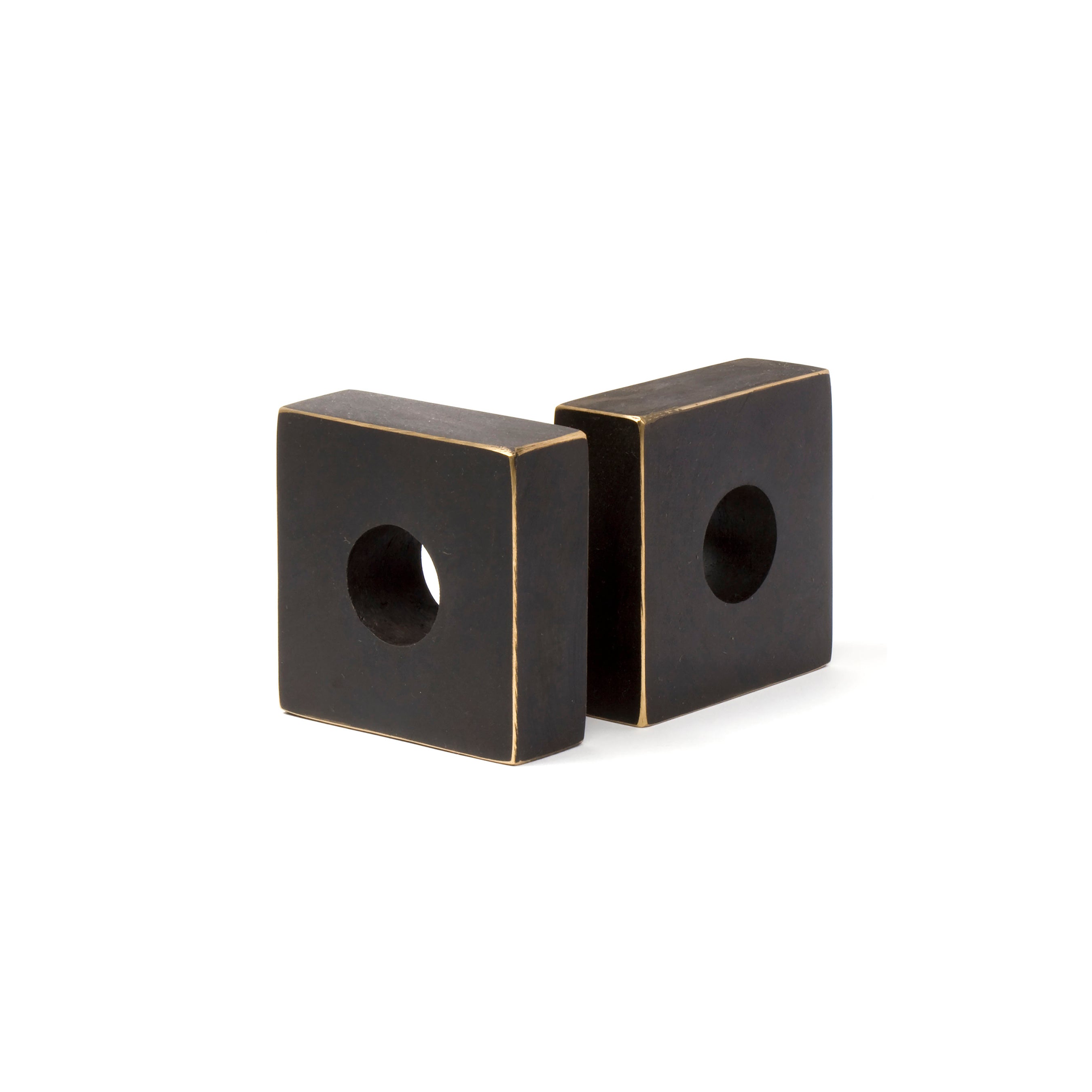 A pair of bookends (#4575) by Werkstätte Carl Auböck, featuring square dark metal with a smooth finish and central circular holes, are displayed upright and slightly angled against a white background, highlighting their sleek geometric elegance.