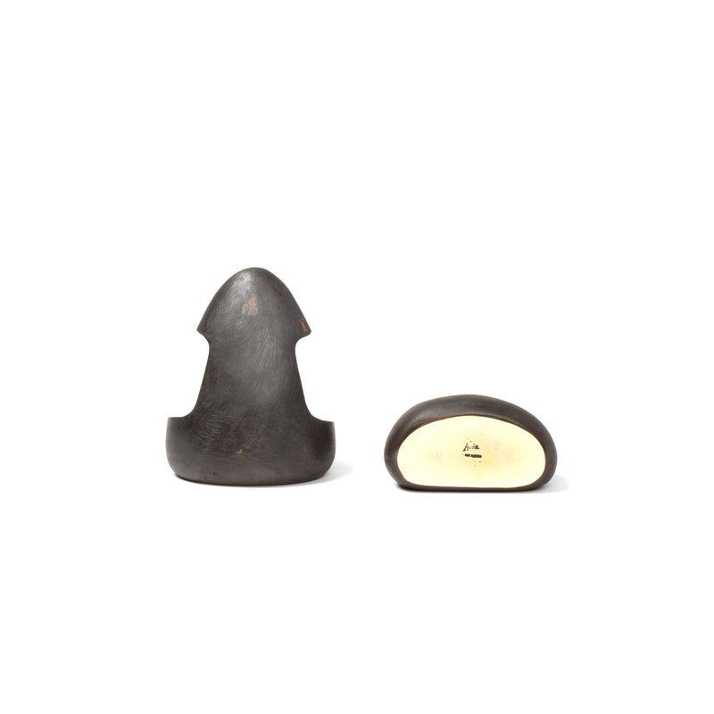 A dark, curved item resembling an arrowhead is depicted beside a similar one on its side, showing a flat, light underside with the esteemed Werkstätte Carl Auböck logo. This is the Pair of Bookends #4637.