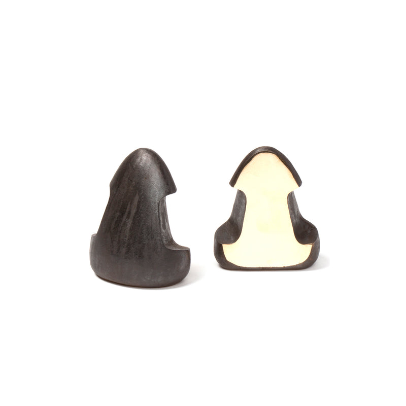 Two black garlic bulbs reminiscent of the Werkstätte Carl Auböck Pair of Bookends #4637, one whole and one halved, are set against a plain white background. The halved bulb reveals a dark interior contrasted by its light outer skin.