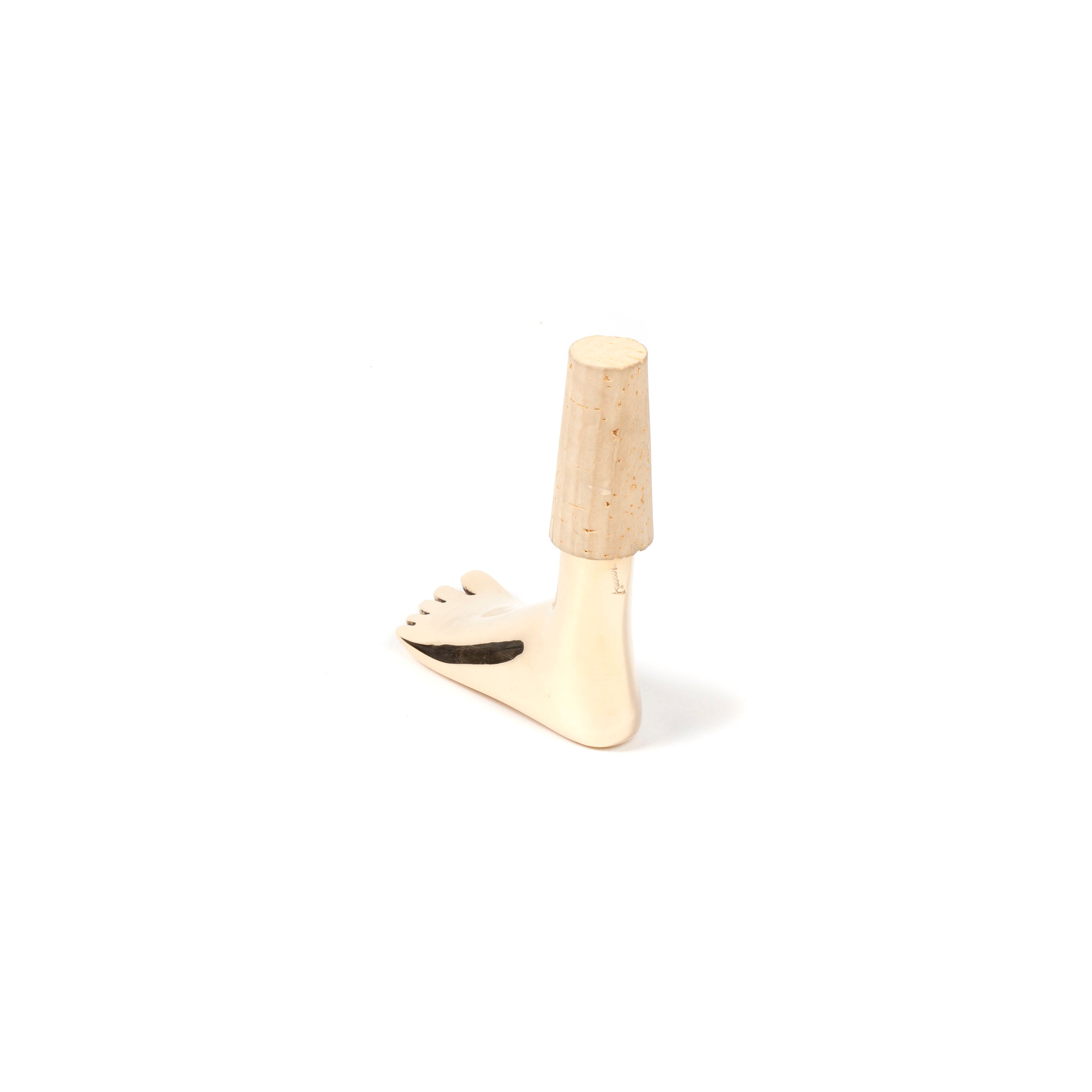 The Corkstopper Foot #4274 by Werkstätte Carl Auböck is a small, white figurine resembling a stylized foot with a cork on top. It stands upright on a white background, featuring intricate toes and a subtle black mark near the base.