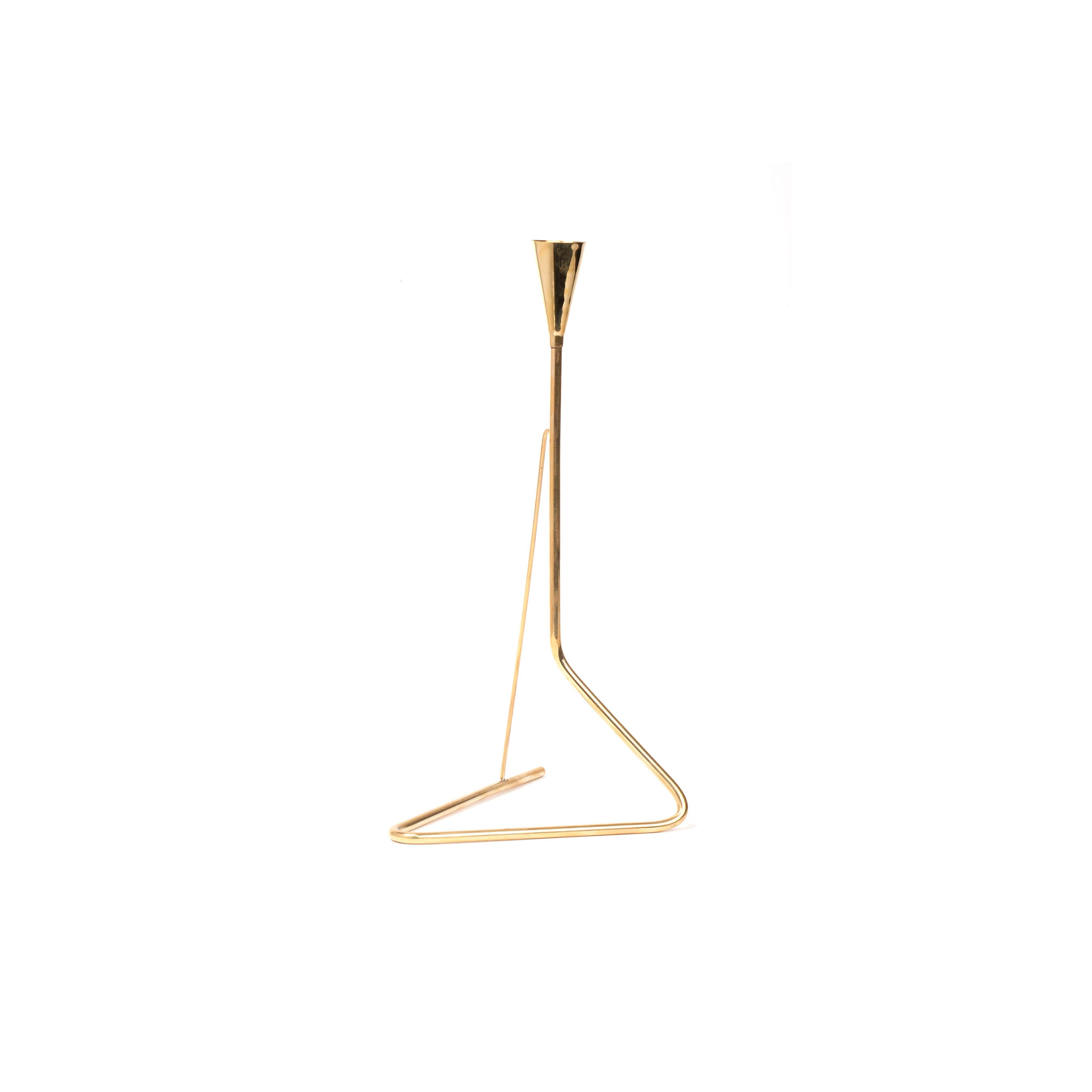 The Candlestick #4103 by Werkstätte Carl Auböck showcases a minimalist design with a sleek triangular base and upward-reaching arm tapering into a narrow candle cup. Its shiny brass finish provides an elegant contrast on a plain white background.