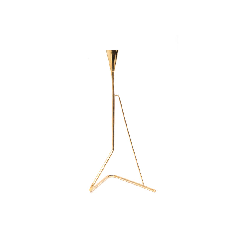 The Candlestick #4103 by Werkstätte Carl Auböck is a minimalist gold metal sculpture with a triangular base and slender vertical rod tapering to a point, elegantly set against a white background.