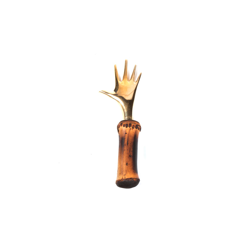 The Corkscrew Hand #4222M by Werkstätte Carl Auböck is a whimsical utensil shaped like a hand with fingers extended, featuring a wooden handle with a slightly charred look that contrasts with its metallic finish, all set against a plain white background.