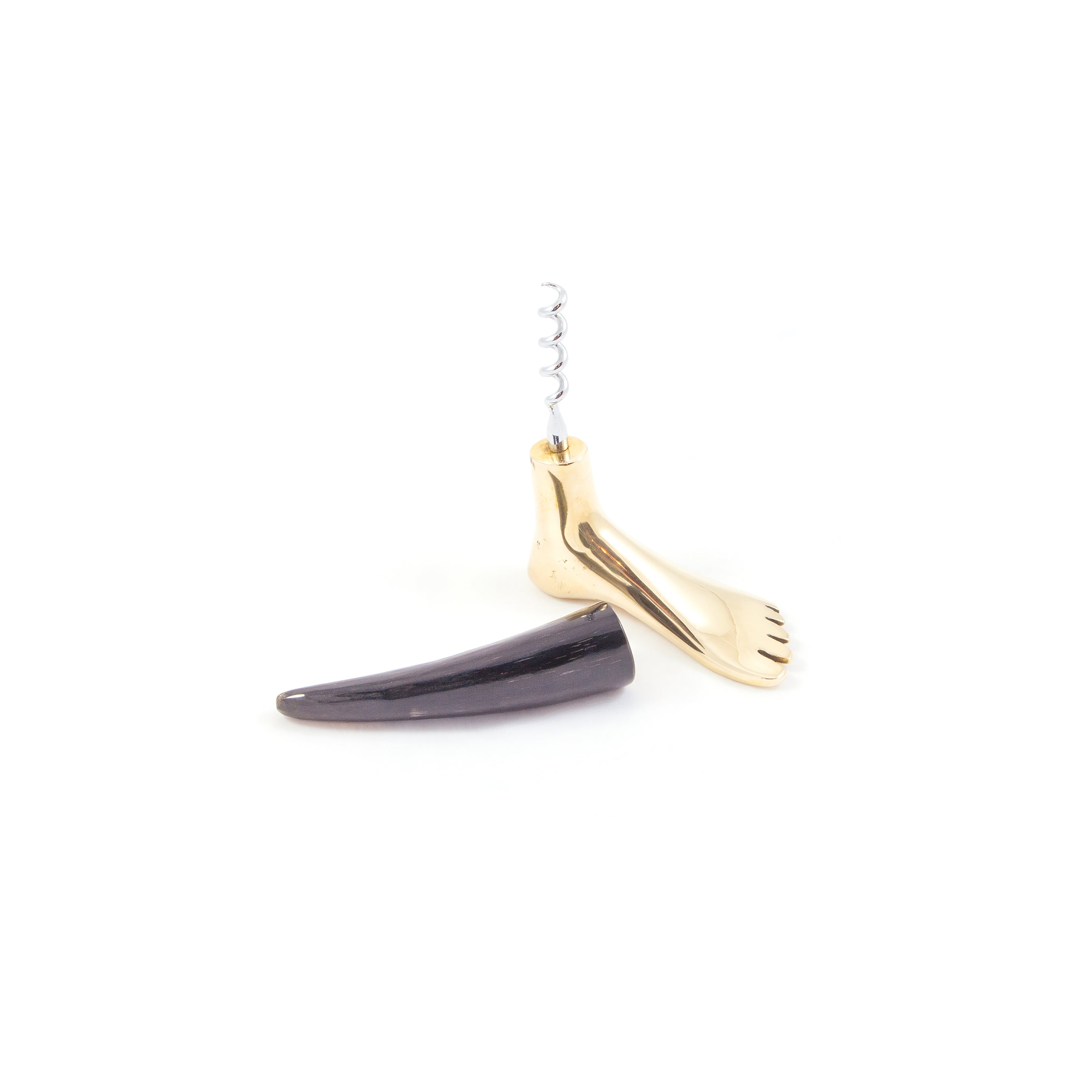 Corkscrew Foot #4275H from Werkstätte Carl Auböck is a gold foot-shaped corkscrew with a coiled metal screw, exuding Carl Auböcks charm. Its paired with a tusk-like dark object, resting elegantly on a white background like art in a Viennese townhouse.