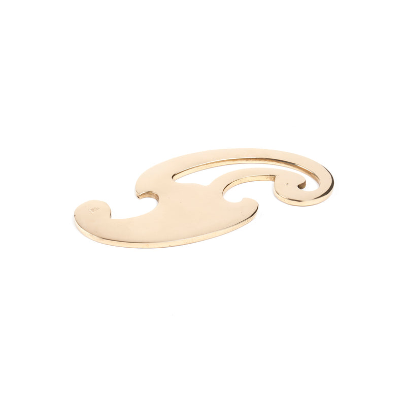 The Paperweight Curve #5085 by Werkstätte Carl Auböck, an ornate gold-hued curve on a white background, evokes the elegant lines of a Viennese townhouse.