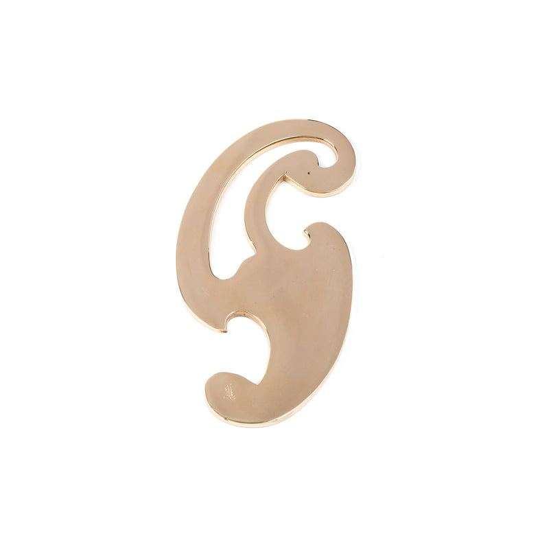 The Paperweight Curve #5085 by Werkstätte Carl Auböck is a gold brooch with smooth curves and cutouts, resembling a stylized G or artistic design against a white backdrop, echoing the elegance of Viennese townhouses.