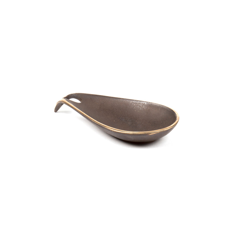Against a white background, the curved ceramic spoon in dark brown boasts a looped handle and smooth finish, akin to Werkstätte Carl Auböcks artistry. With its pointed end and subtle golden trim, it evokes the elegance of a Viennese townhouse.