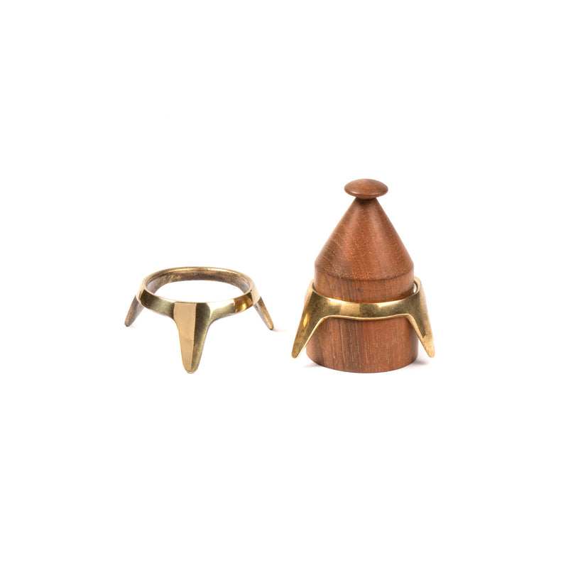 The Egg Cup #4153-1 by Werkstätte Carl Auböck features a wooden cone with a pointed tip, flanked by two brass trivet rings. One ring is positioned horizontally, and the other rests at the base. This minimalist design captures Viennese townhouse charm against a white background.