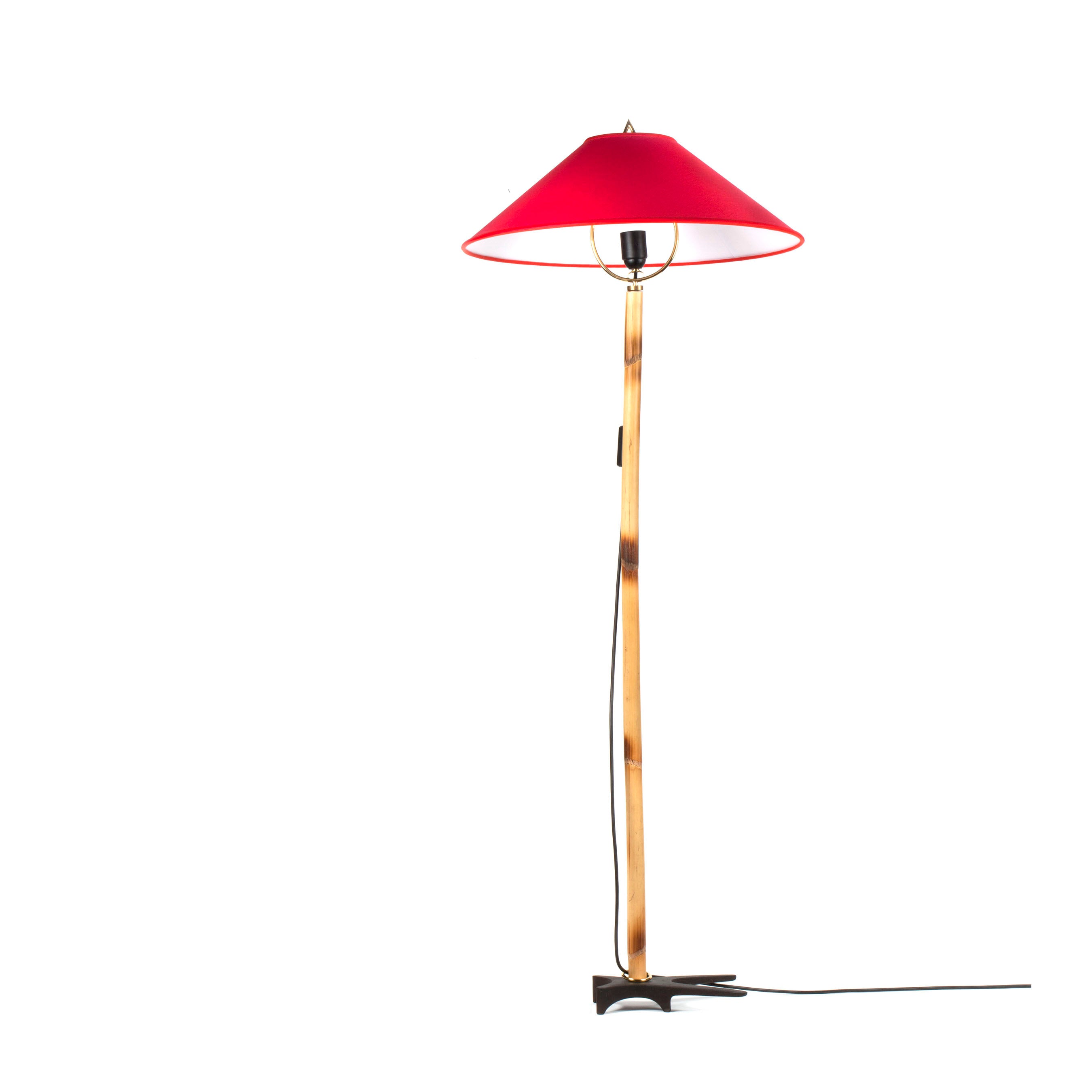 The Floorlamp Butterfly #3740 by Werkstätte Carl Auböck features a tall wooden base with a vibrant red conical shade, supported by a black star-shaped metal base. A visible black cord elegantly extends from the base, all set against a plain white backdrop.