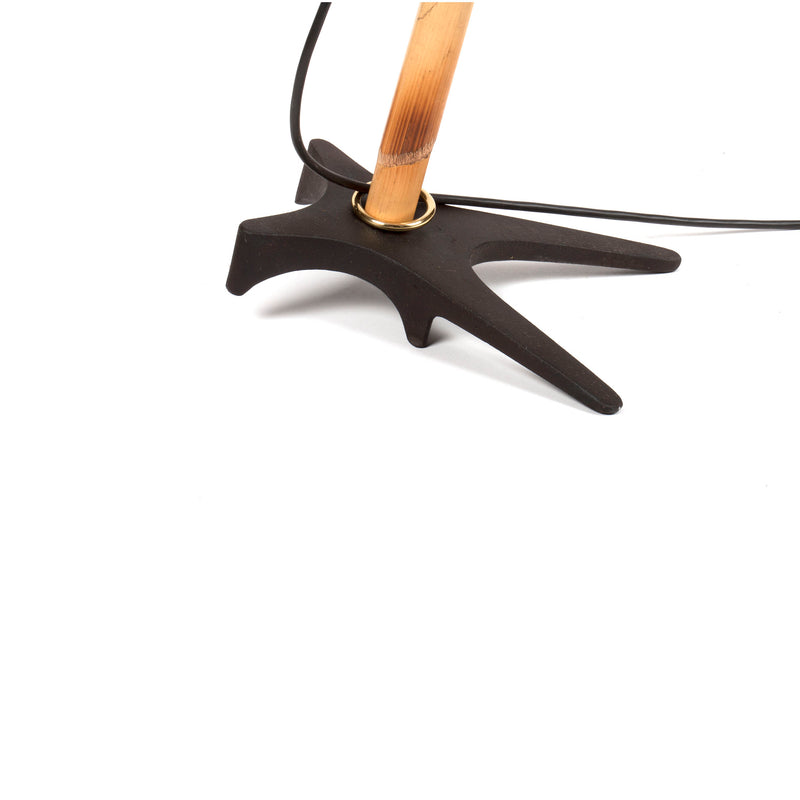 A close-up of the Floorlamp Butterfly #3740 by Werkstätte Carl Auböck showcases a modern tripod-style base with angular black legs and a wooden pole, complemented by a sleek black cord. The plain white background highlights its minimalist elegance.