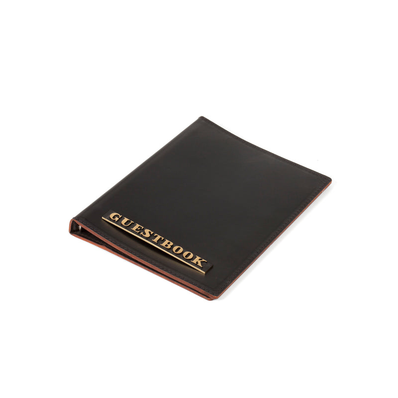 The Guestbook #5116/1 by Werkstätte Carl Auböck is a black leather guestbook with GUESTBOOK in gold lettering on its cover, set against a plain white background.