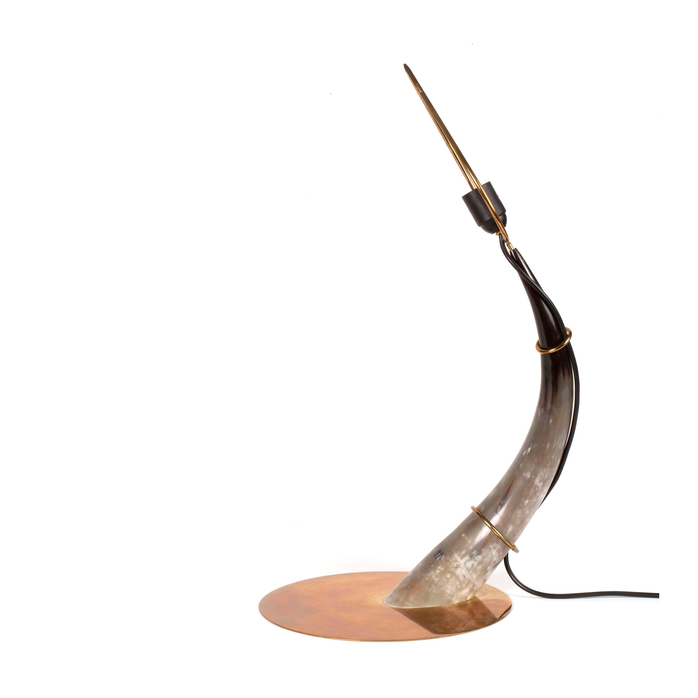 The Table lamp Horn #7255 by Werkstätte Carl Auböck features a curved goat horn design on a circular copper base with a slim lightbulb, and a black cord, blending minimalist and rustic elements reminiscent of the Triennale di Milano 1954.