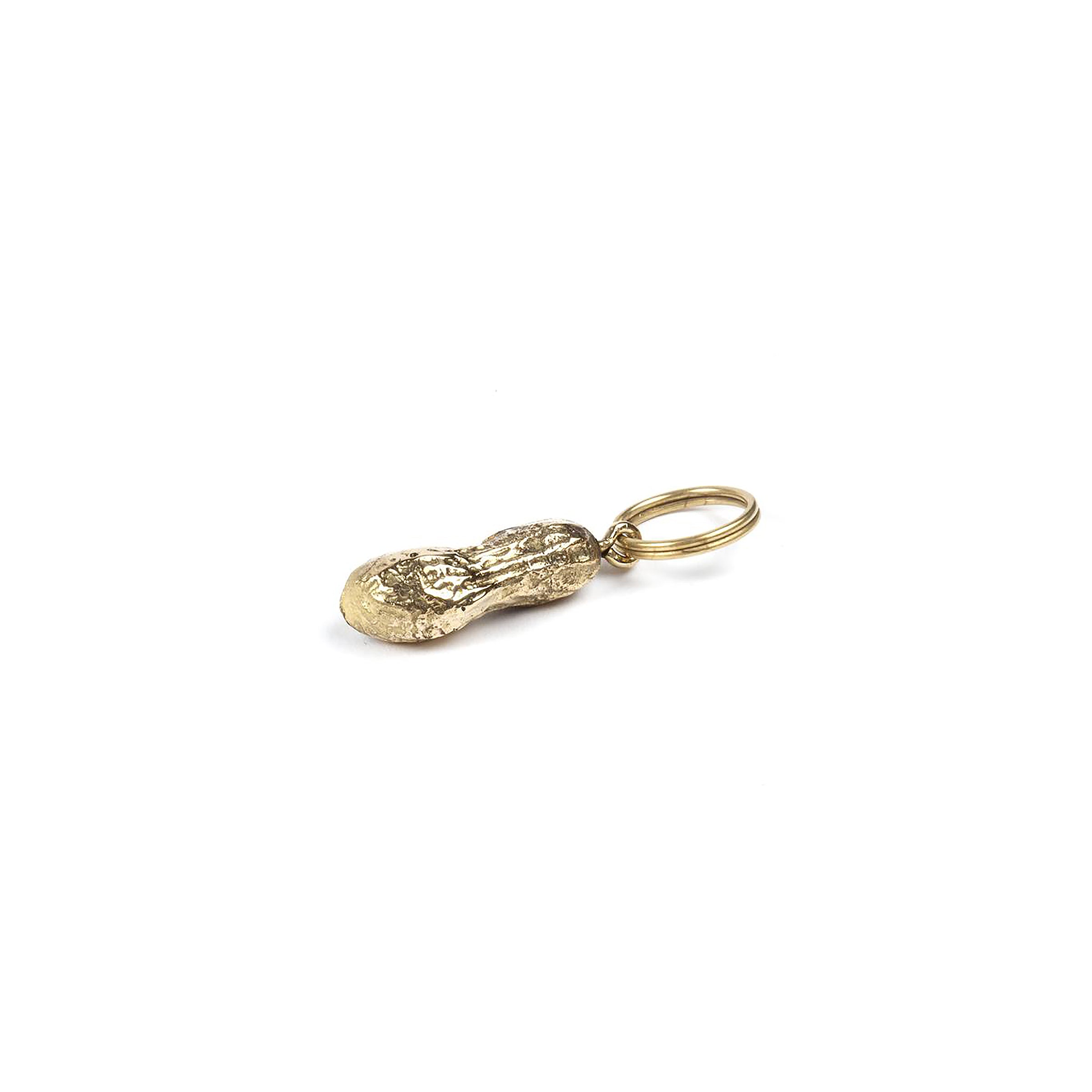 The Keyring Peanut #5617 by Werkstätte Carl Auböck is a small, gold-colored keychain in a peanut shape with a textured surface and an attached circular ring, set against a plain white background.