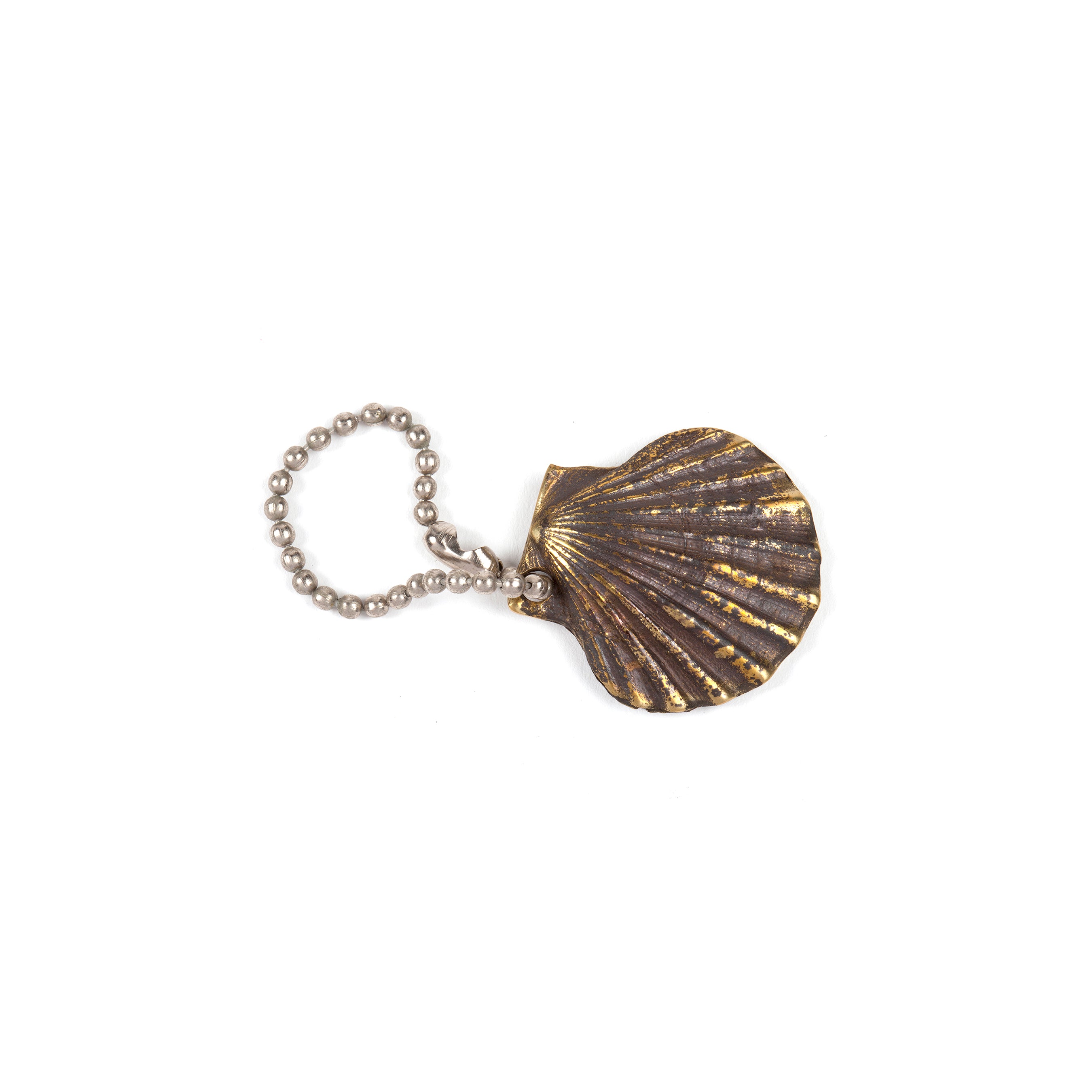 A brass-colored Keyring Shell #5663 by Werkstätte Carl Auböck, featuring detailed ridges and a weathered look, hangs on a silver ball chain reminiscent of a Viennese townhouse artifact.