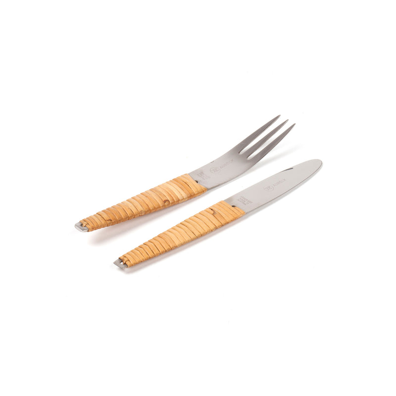 A close-up of the Werkstätte Carl Auböck Knife and Fork #4244 set shows a fork with three tines and a knife with a smooth blade, both featuring shiny metal finishes and light tan rattan-wrapped handles, elegantly displayed on a plain white background akin to Triennale di Milano exhibits.