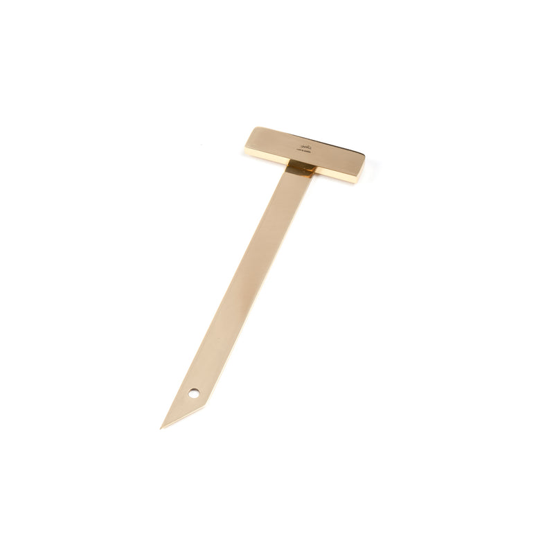 The Paperweight T-Square #6086 by Werkstätte Carl Auböck is a gold metal object with a T-shaped design, pointed end, and a small hole near the tip.