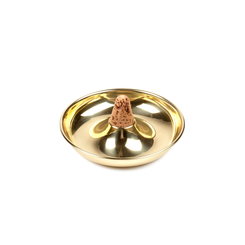 The Pipe Ashtray #7202 by Werkstätte Carl Auböck features a conical incense stick at the center, with a shiny surface that beautifully showcases the light brown stick with dark speckles against a plain white background.