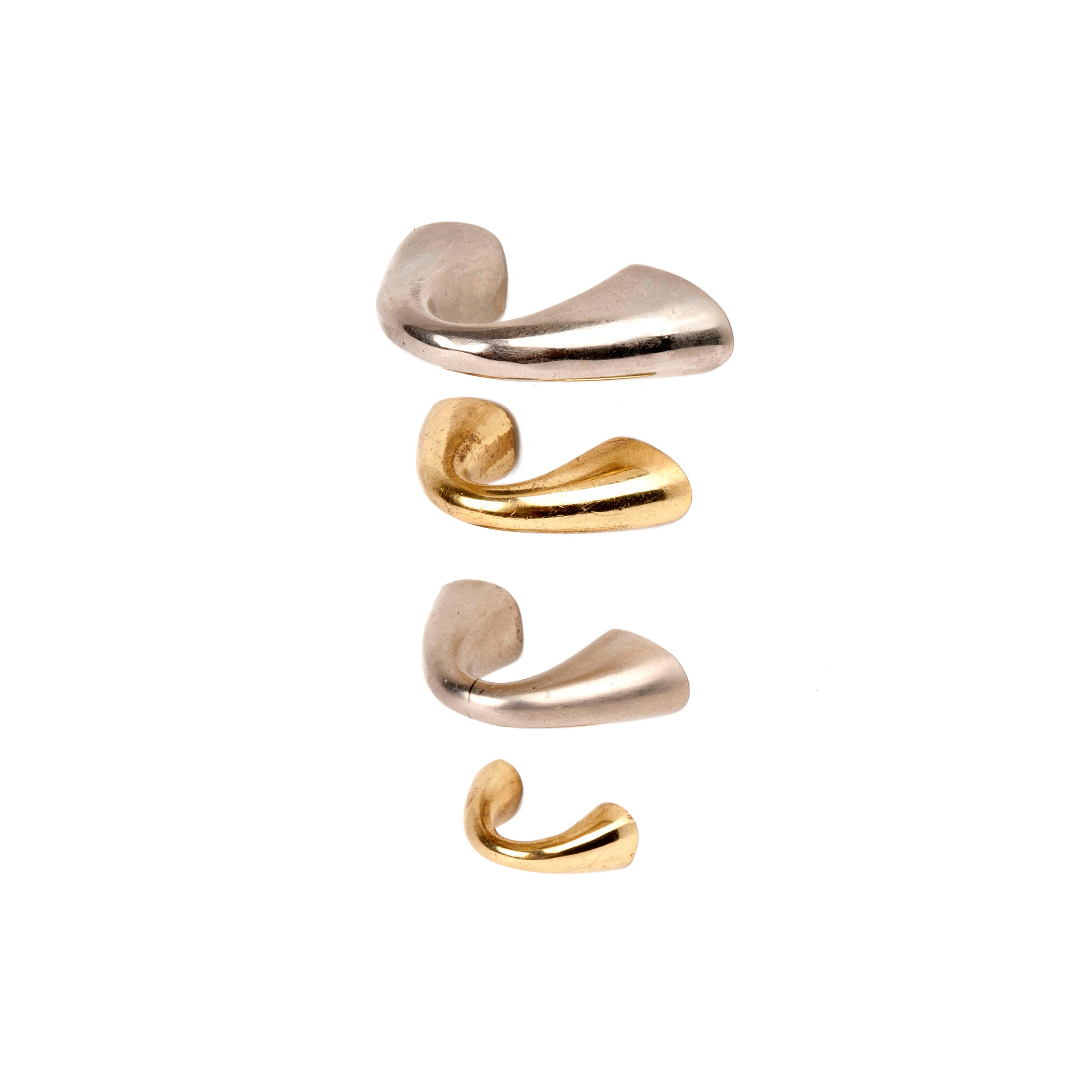 A set of four abstract, wave-like metal sculptures from Werkstätte Carl Auböck, known as Puller #9030 #9031, is arranged vertically against a white background. Two silver pieces on the top and bottom are complemented by two gold pieces in the middle.