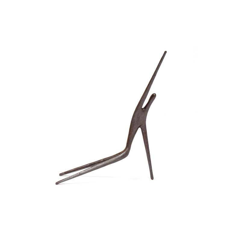 Sculpture #4057 by Werkstätte Carl Auböck features a minimalist, dark metal human figure in a dynamic leaning pose. Its abstract form with elongated limbs and a smooth surface suggests movement and balance against a plain white background.