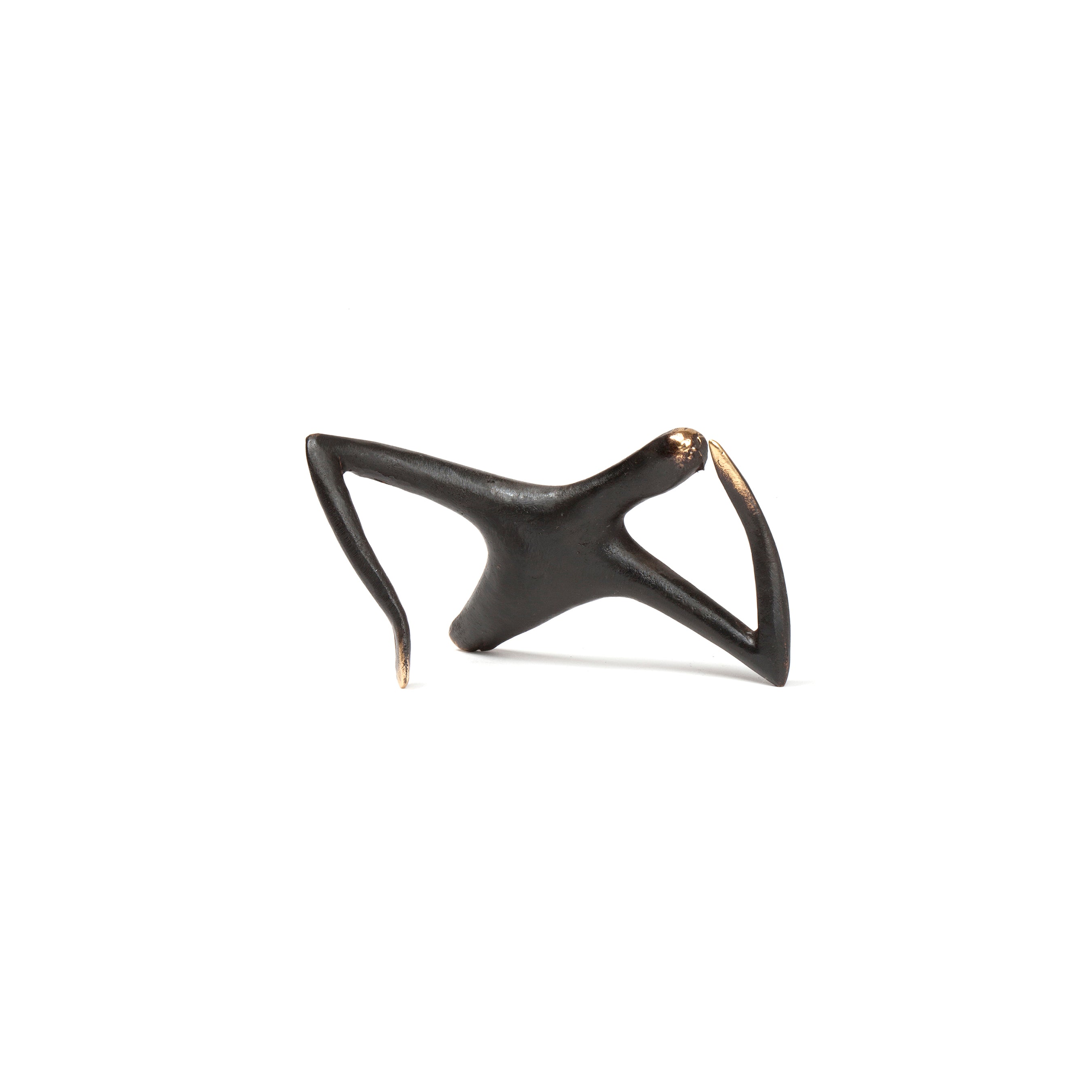 The Optimist or Pessimist #4059 by Werkstätte Carl Auböck is a small, abstract black sculpture with three elongated, curved arms emerging from a central point against a white background.