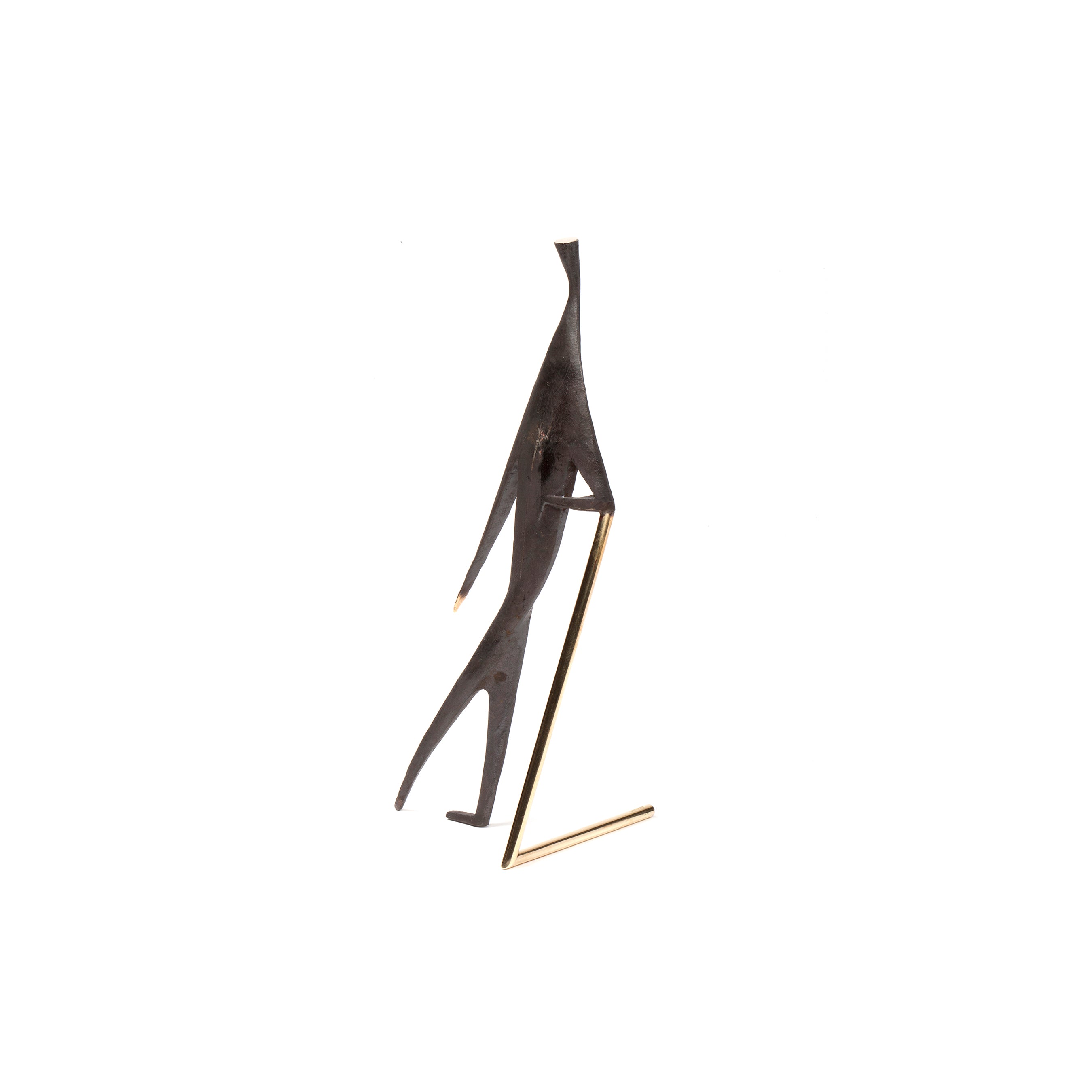 Sculpture #4060 by Werkstätte Carl Auböck features a minimalist black metal human figure, leaning left with elongated limbs. A thin golden rod supports the piece diagonally from below. Set against a white background, it echoes the refined style of Carl Auböck.