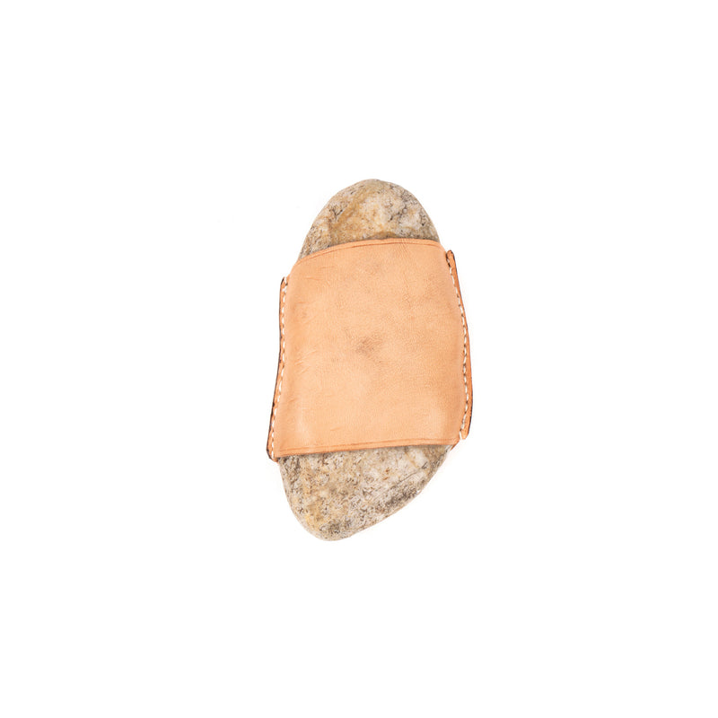 Stone #4339 by Werkstätte Carl Auböck features a stone wrapped in a tan leather band, exuding timeless elegance against a white background.
