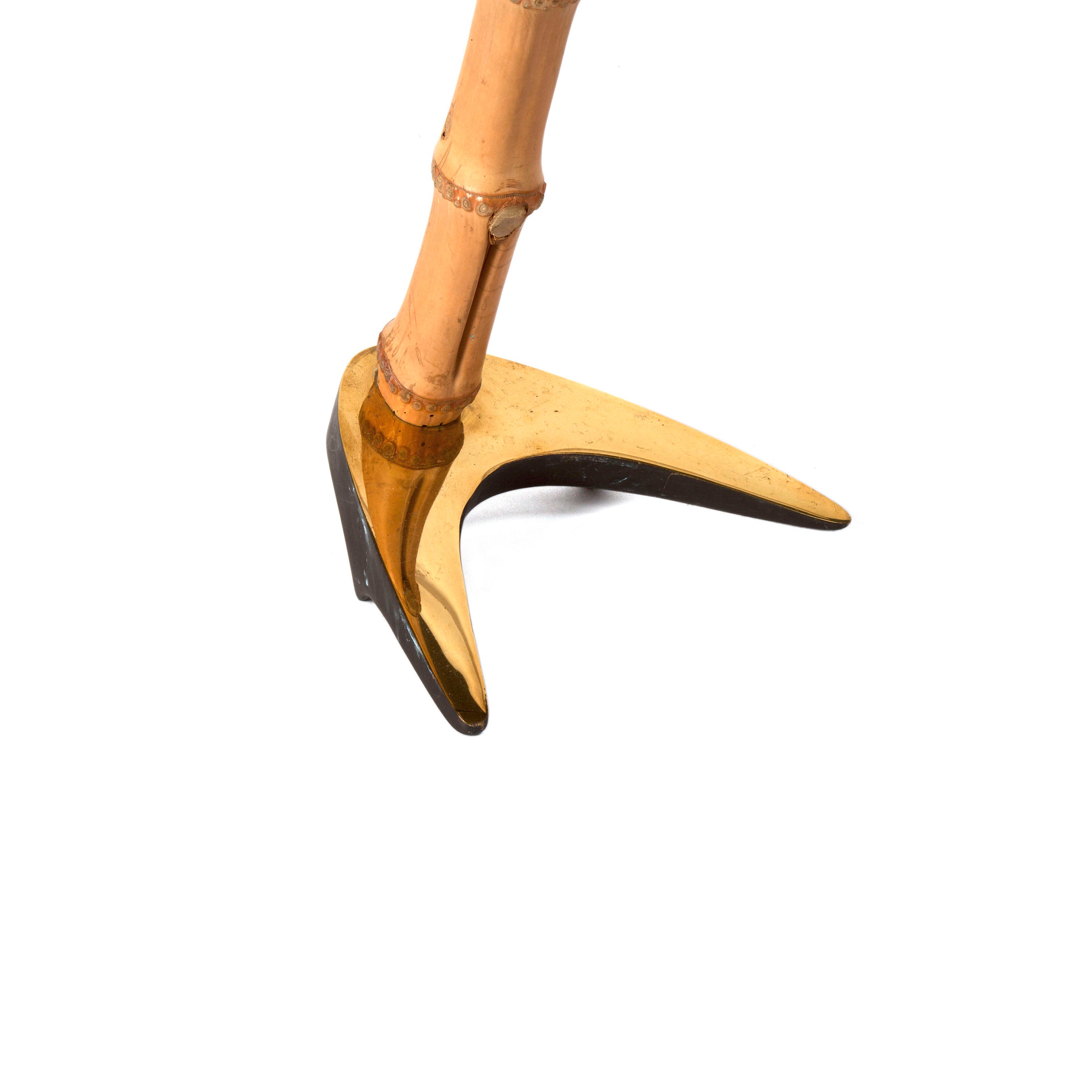 Close-up of a decorative bird leg in the style of Wiener Bronzen with a bamboo-like texture and golden black webbed foot. The design, akin to Viennese craftsmanship, features segmented joints and casts a shadow on a white background. (Table Lamp Horse Shoe #3741 by Werkstätte Carl Auböck).