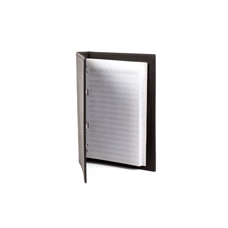 The Telephone Register #5116/1 by Werkstätte Carl Auböck, a dark leather-bound address book, opens to Wichtige Rufnummern (Important Numbers). Its sleek design with visible stitching echoes the artistry of a Viennese townhouse set against a plain white background.