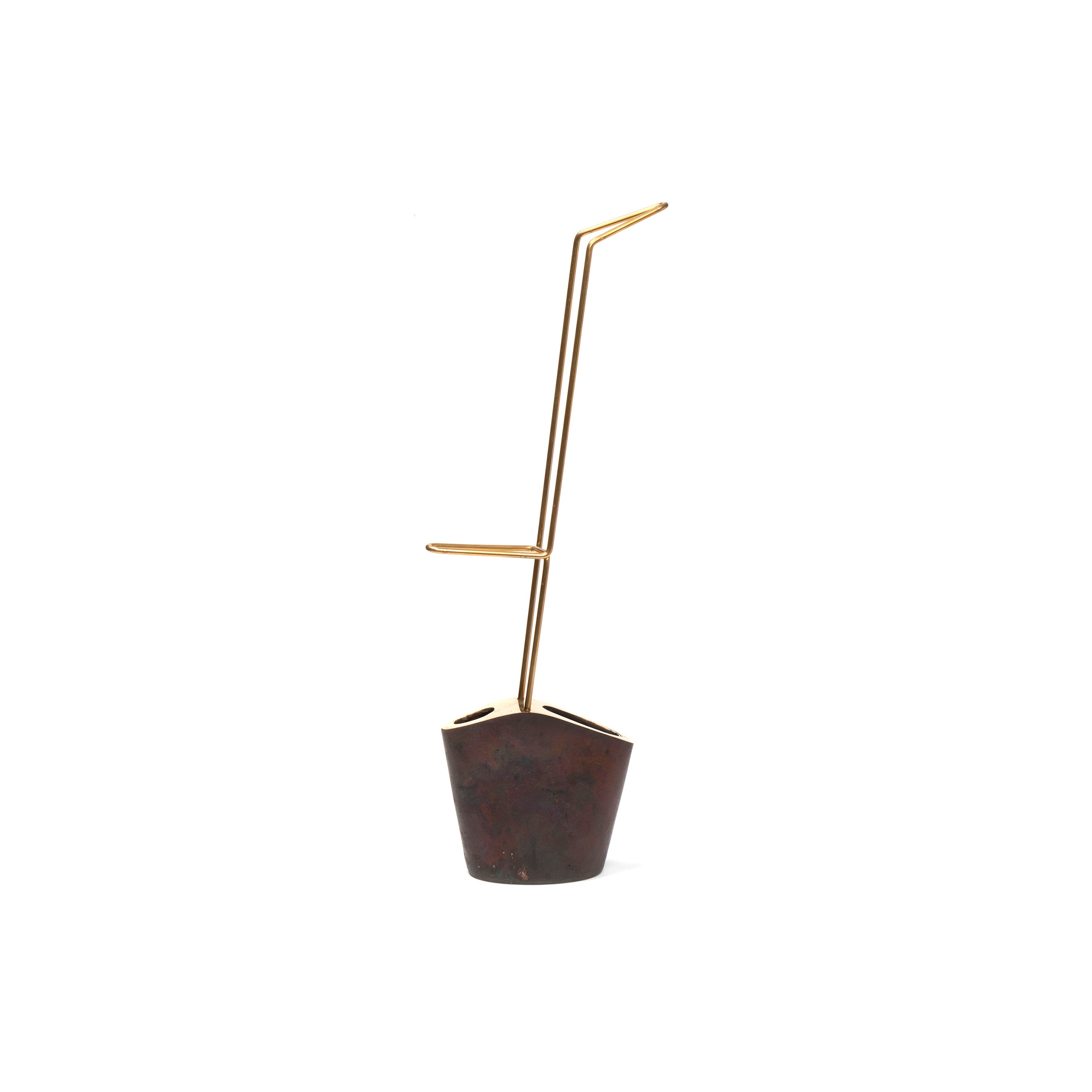 The Vase #3853 by Werkstätte Carl Auböck features a minimalist metal sculpture with a rust base and two thin gold rods, evoking the geometric style seen at the Triennale di Milano against a white backdrop.