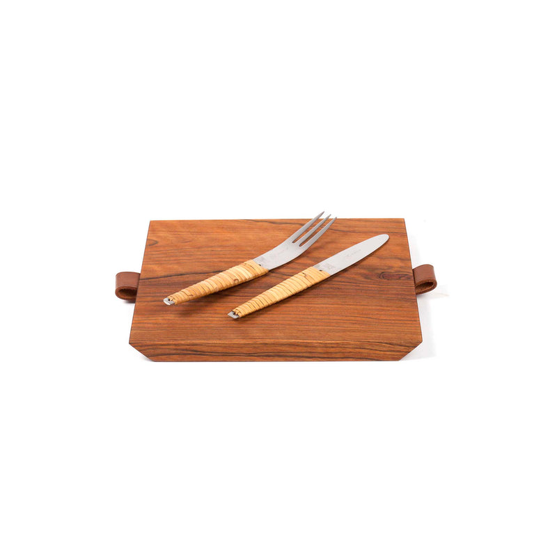 The Walnut Board with Knife and Fork #4363-1 by Werkstätte Carl Auböck features a wooden cutting board with leather handles, showcasing a stainless steel fork and knife with wooden handles, elegantly set against a white background.