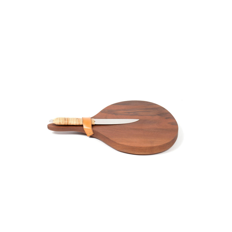 Against a white background is the Walnut Board with Cheeseknife #4363-2, a round wooden board featuring a leather strap. The knife, with its wooden handle, captures the meticulous design of Werkstätte Carl Auböck’s Viennese craftsmanship.
