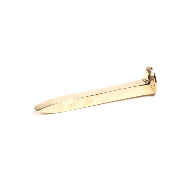 The Paperweight Railroadnail #5038 by Werkstätte Carl Auböck resembles a gold-toned flat key with a thin, elongated body and rounded grip, elegantly positioned horizontally against a white background.