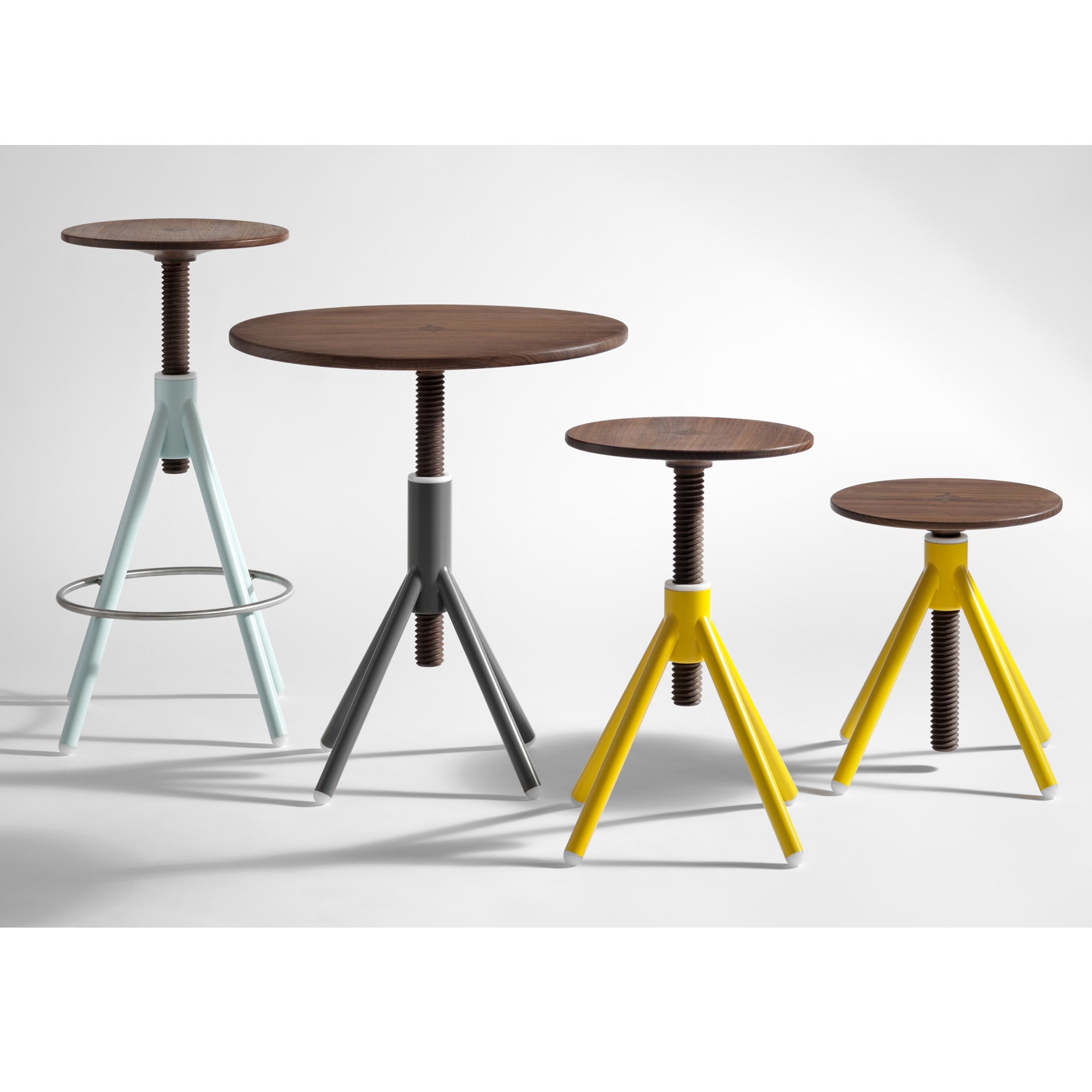 Four adjustable-height round stools from Coordination Berlin’s Thread Family - Bistro Table feature oak seats on spiral welded steel bases with tripod legs in pastel blue, gray, and yellow. The tallest stool includes a footrest ring. They are displayed on a plain backdrop.