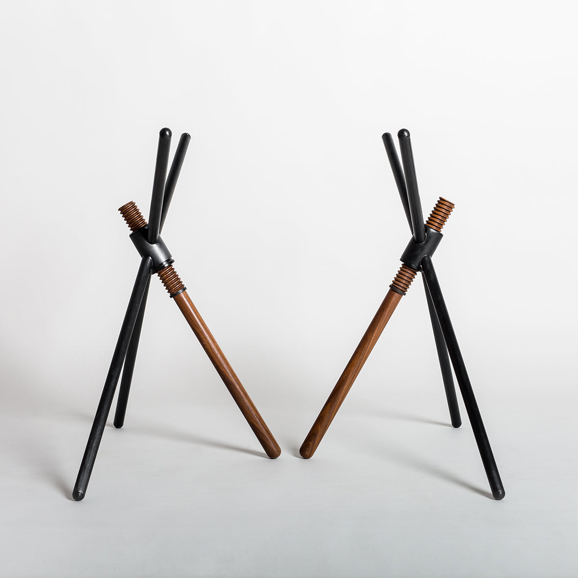 Two minimalist sculptures from Coordination Berlin showcase contemporary design with three black rods as a tripod, one central brown rod, and a metal connector. Crafted from vertical wooden rods on a white background, they reflect the innovation of Thread X.
