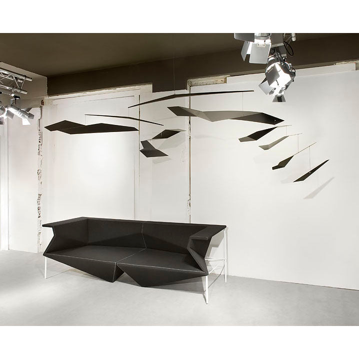In a gallery of contemporary architecture, the Coordination Berlin Crowd mobile features abstract flat, dark shapes that harmonize with a geometric black sofa. Spotlights enhance the sleek aesthetic of this modern art installation.