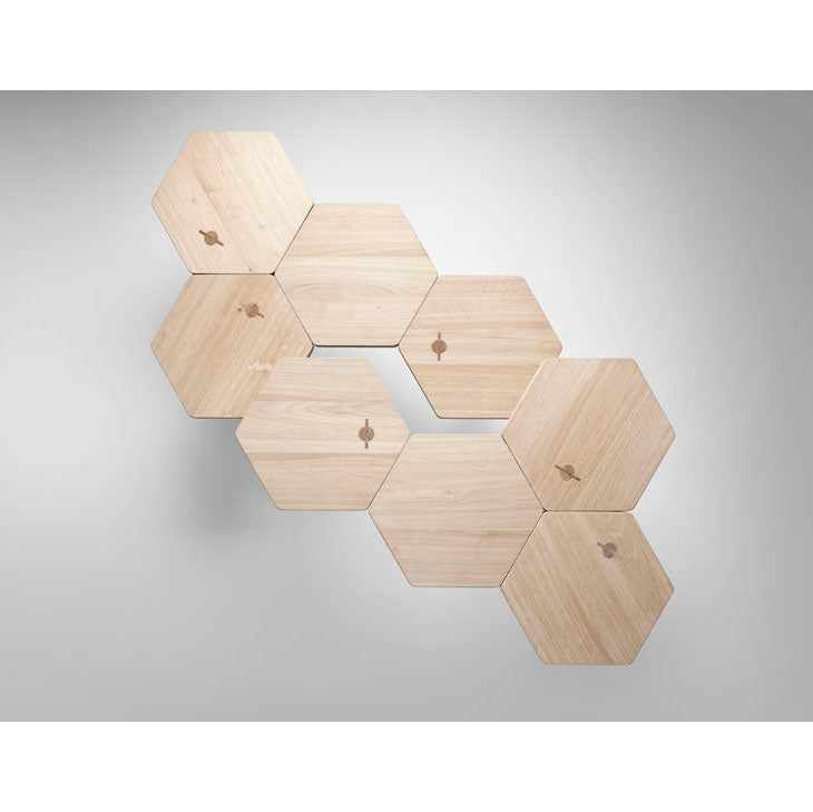 Lean Tables by Coordination Berlin, crafted from local oak, create a honeycomb pattern against a light grey backdrop. Each table reflects contemporary design and features a distinctive small keyhole.